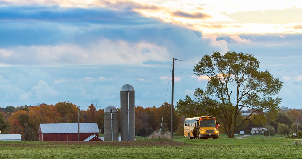 School bus running on autogas coming down a country road in front of a farm