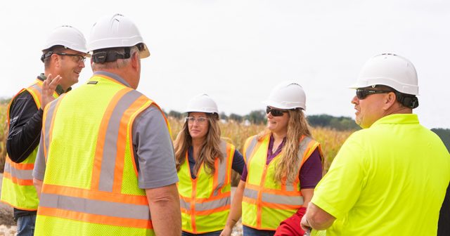 five people in reflective vests in a field, two of them women, discussing farm safety and networking